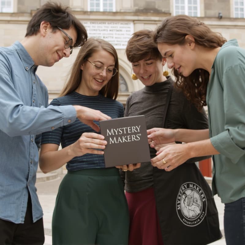 Four people are opening a Mystery Makers box in the courtyard of Christiansborg Palace