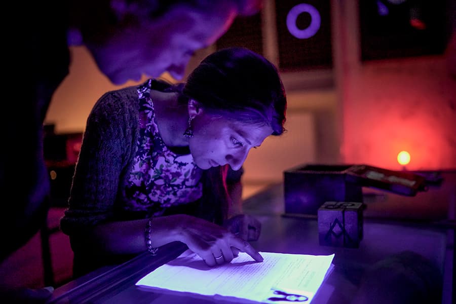 Two participants are reading a document in violet light at The Crime Scene on Grønningen